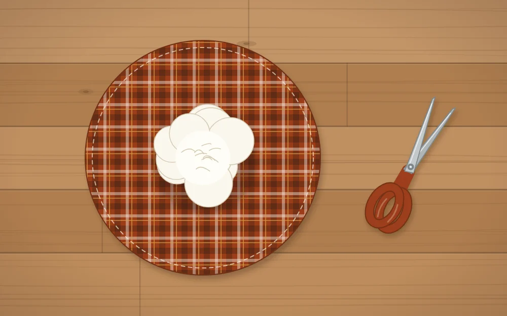 A round piece of fabric laid flat with a mound of white stuffing in the center and scissors beside it
