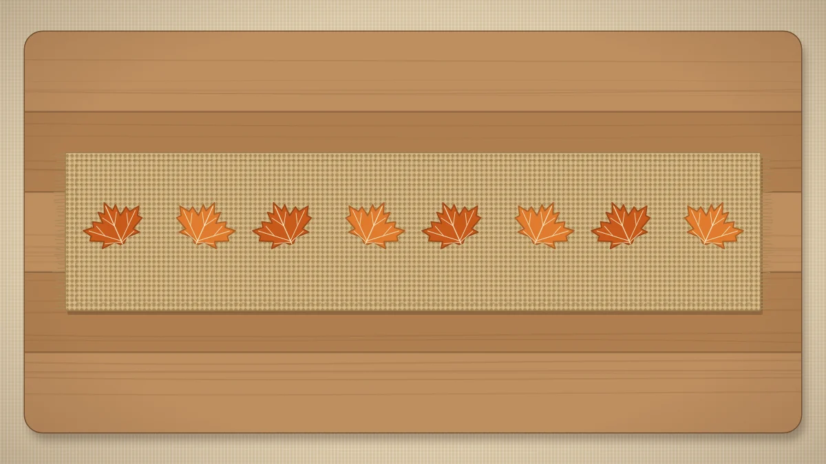 A burlap runner with fringed ends and a row of stamped orange leaves along its center, lying down the middle of a wooden table