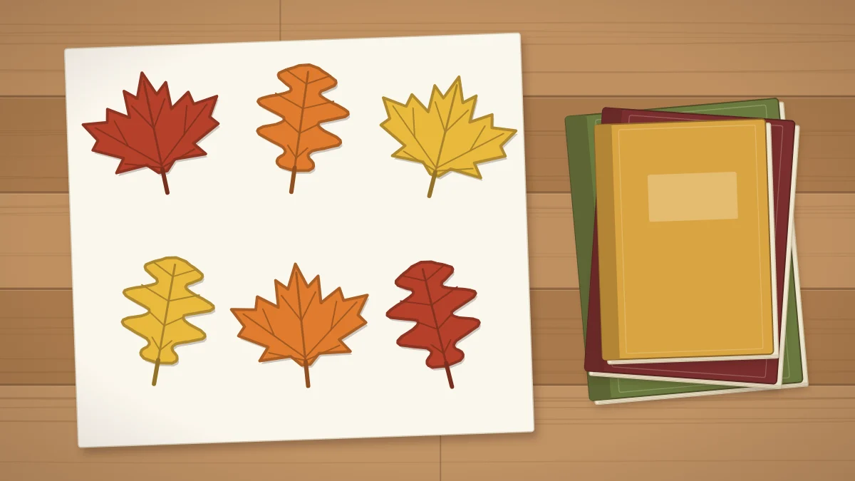 Pressed maple and oak leaves in red, orange and yellow arranged on a sheet of paper beside a stack of heavy books