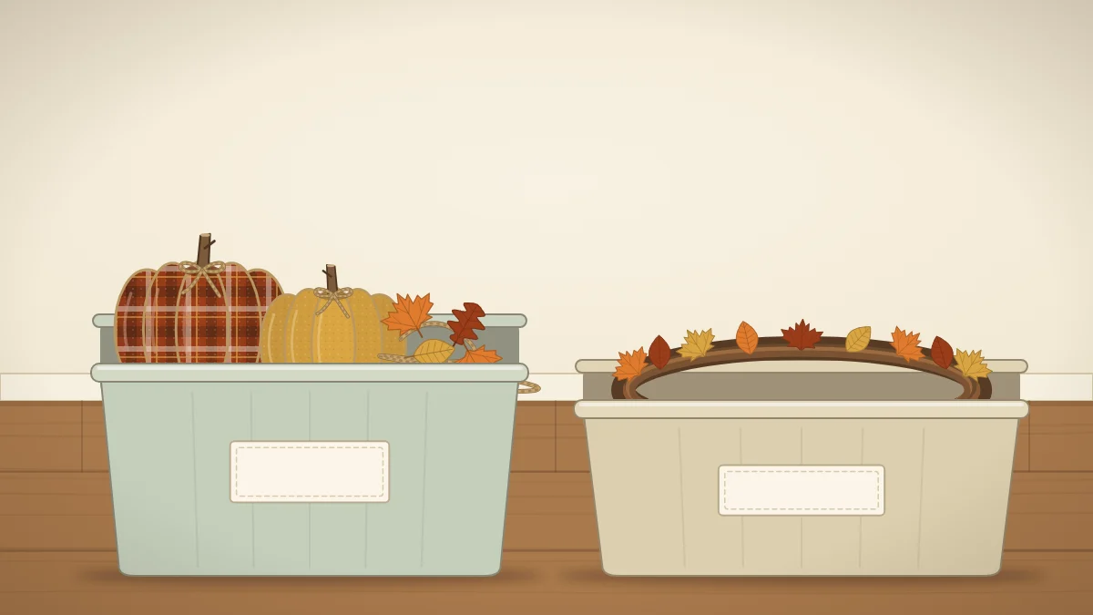Two open storage bins holding fabric pumpkins, a folded garland and a wreath laid flat, with blank labels on the front