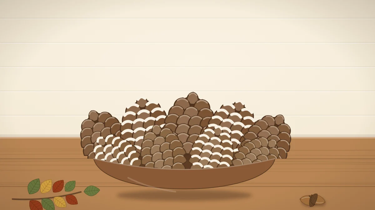 A shallow wooden bowl filled with pinecones, some with white-painted tips, beside two acorns and a sprig of leaves